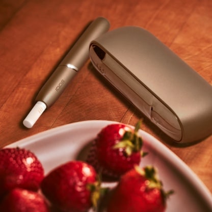 An IQOS device next to a bowl of fruit.