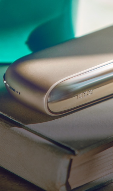 A gold IQOS device and holder on a closed book.