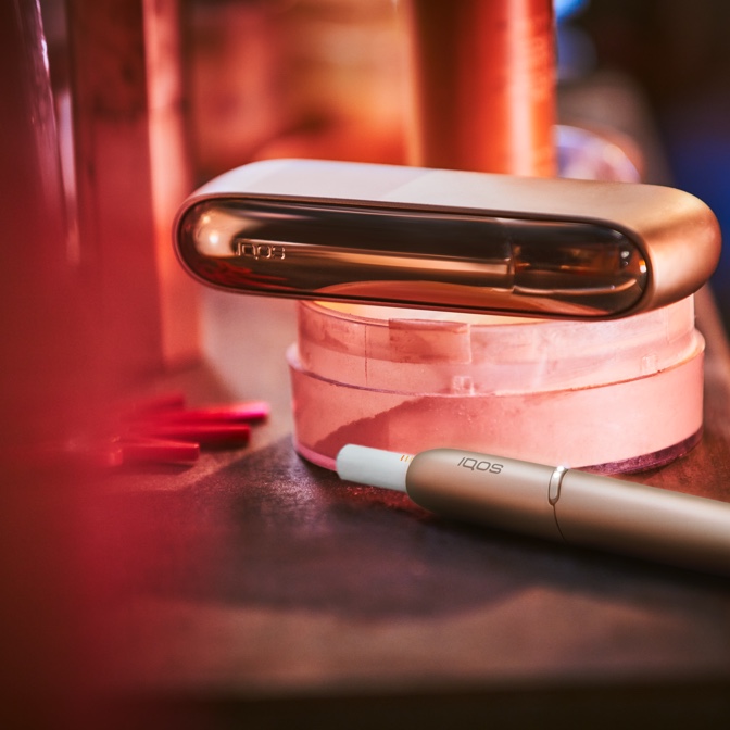 Gold IQOS charger on round box on table, holder with HEETS next to it