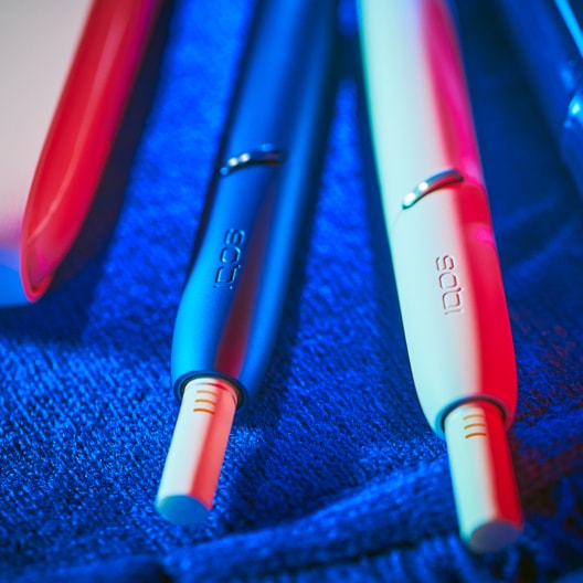 A blue and a white IQOS device on a blue surface.