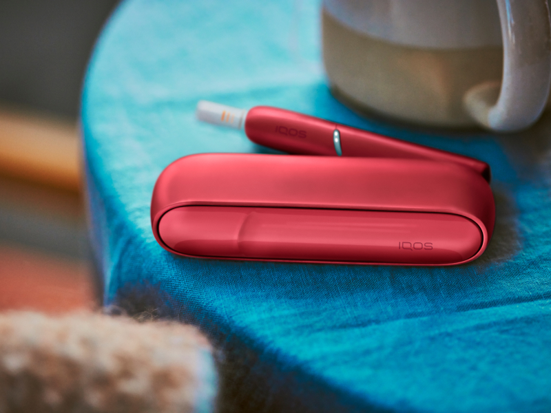 IQOS Originals Duo holder with HEETS stick and pocket charger in red color, on a coffee table.