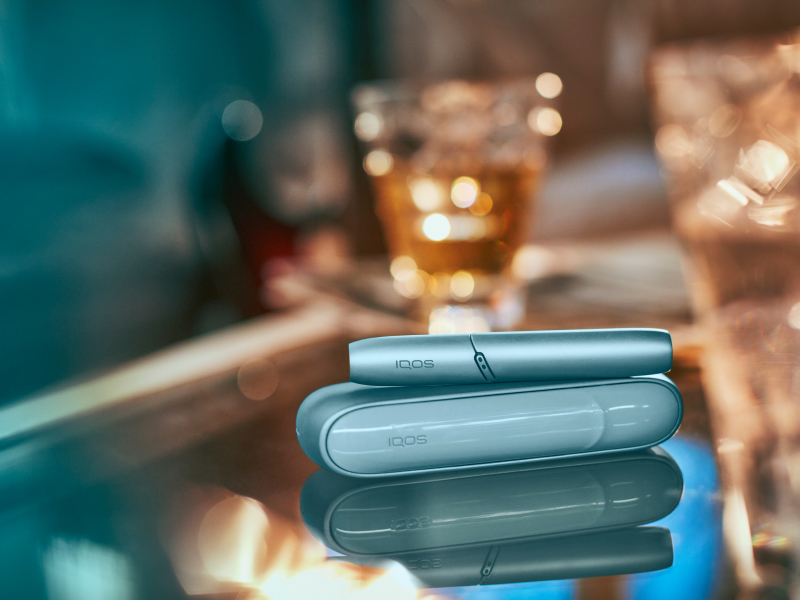 IQOS Originals Duo Holder and Pocket Charger in black color on a glass table.