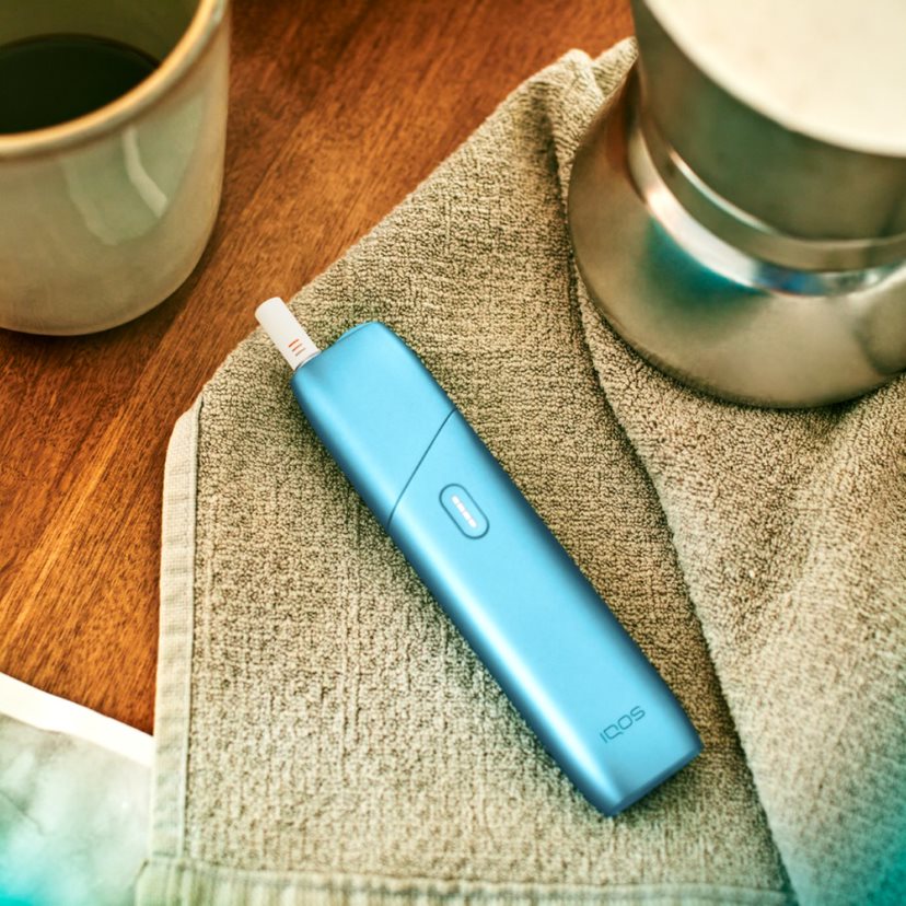 Turquoise IQOS Originals One heated tobacco device on a fabric table mat.
