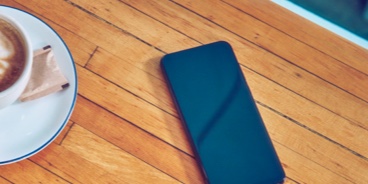 A smartphone on a table next to a cup of coffee.