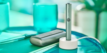 A charging Jade Green IQOS ILUMA PRIME device on a table.