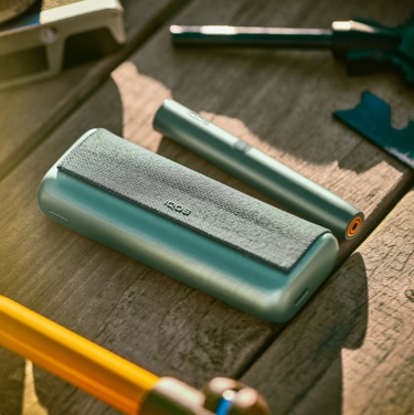 A Jade Green IQOS ILUMA PRIME Holder and Pocket Charger on a wooden table.
