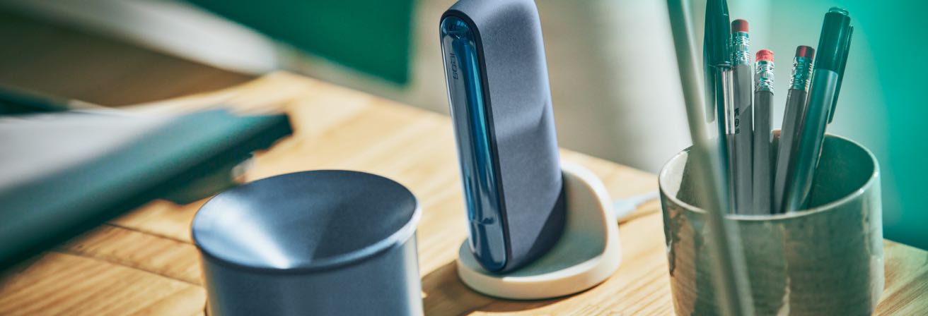 An IQOS ILUMA Pocket Charger in a charging dock with an IQOS Tray nearby.