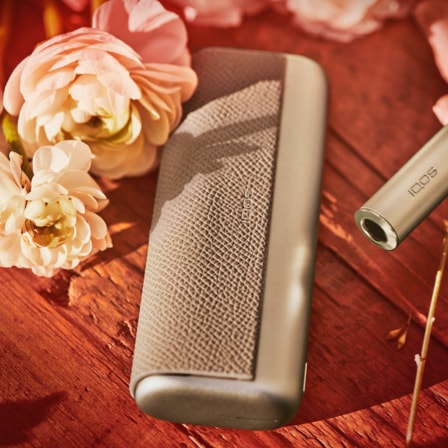 An IQOS ILUMA device on a table surrounded by flowers.