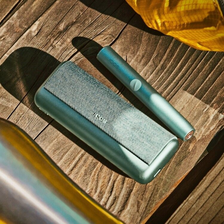 A Jade Green IQOS ILUMA PRIME Holder and Pocket Charger on a wooden table.